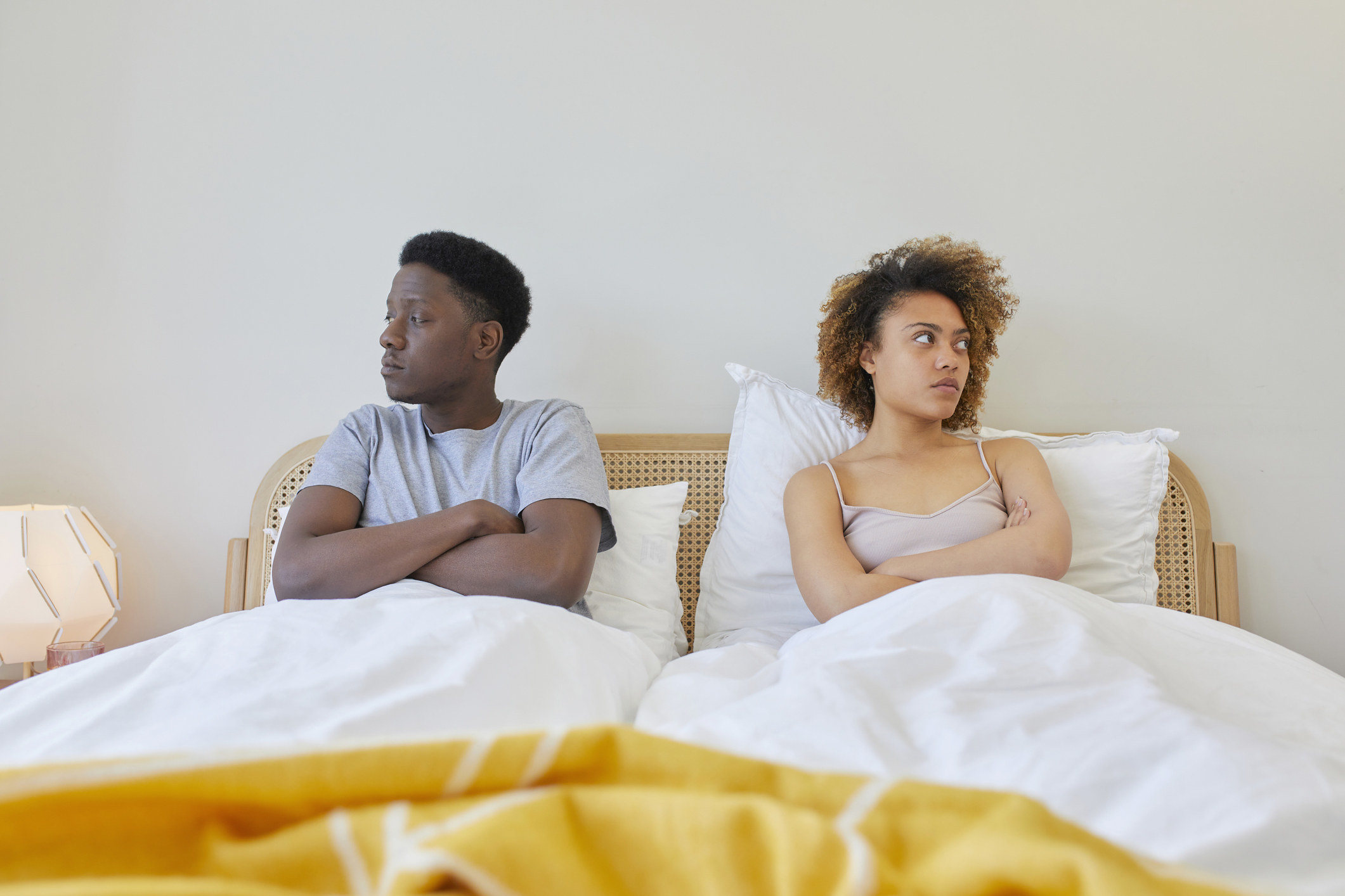 a couple sitting in bed with crossed arms and looking in opposite directions