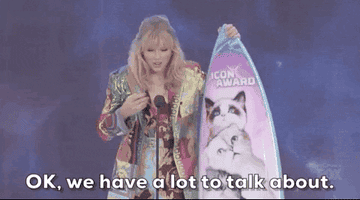 taylor swift holding her teen choice icon award aka a surfboard with her cats&#x27; faces on it and saying &quot;ok we have a lot to talk about&quot;