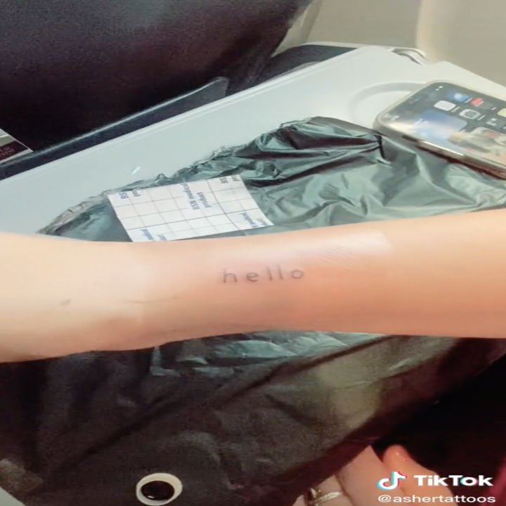 Screenshot from a video by TikTok user @luckyboytattoo of a fresh tattoo that says "Hello" on an arm