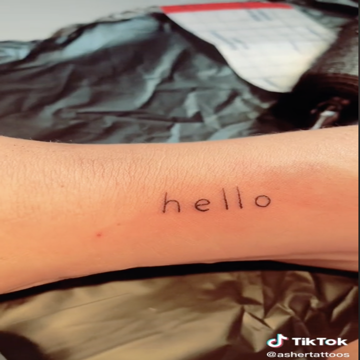 Screenshot from a video by TikTok user @luckyboytattoo of a fresh tattoo that says "Hello" on an arm