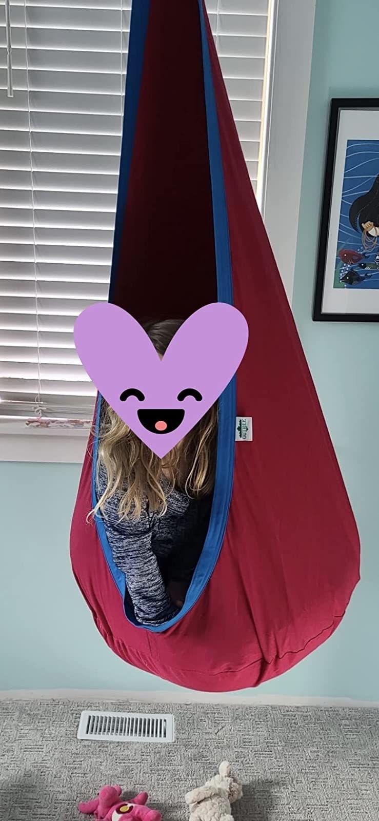 reviewer photo of their kid (with a heart graphic covering their face) in a hanging hammock chair