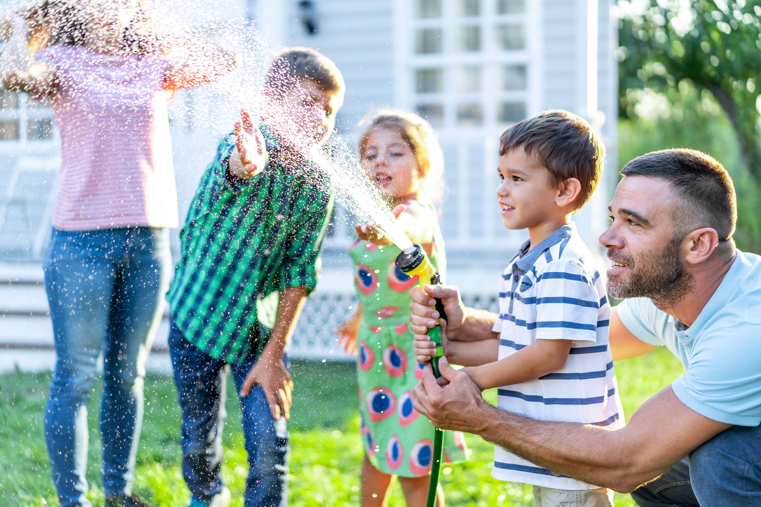 Three siblings and their parents spray a garden hose on their lawn