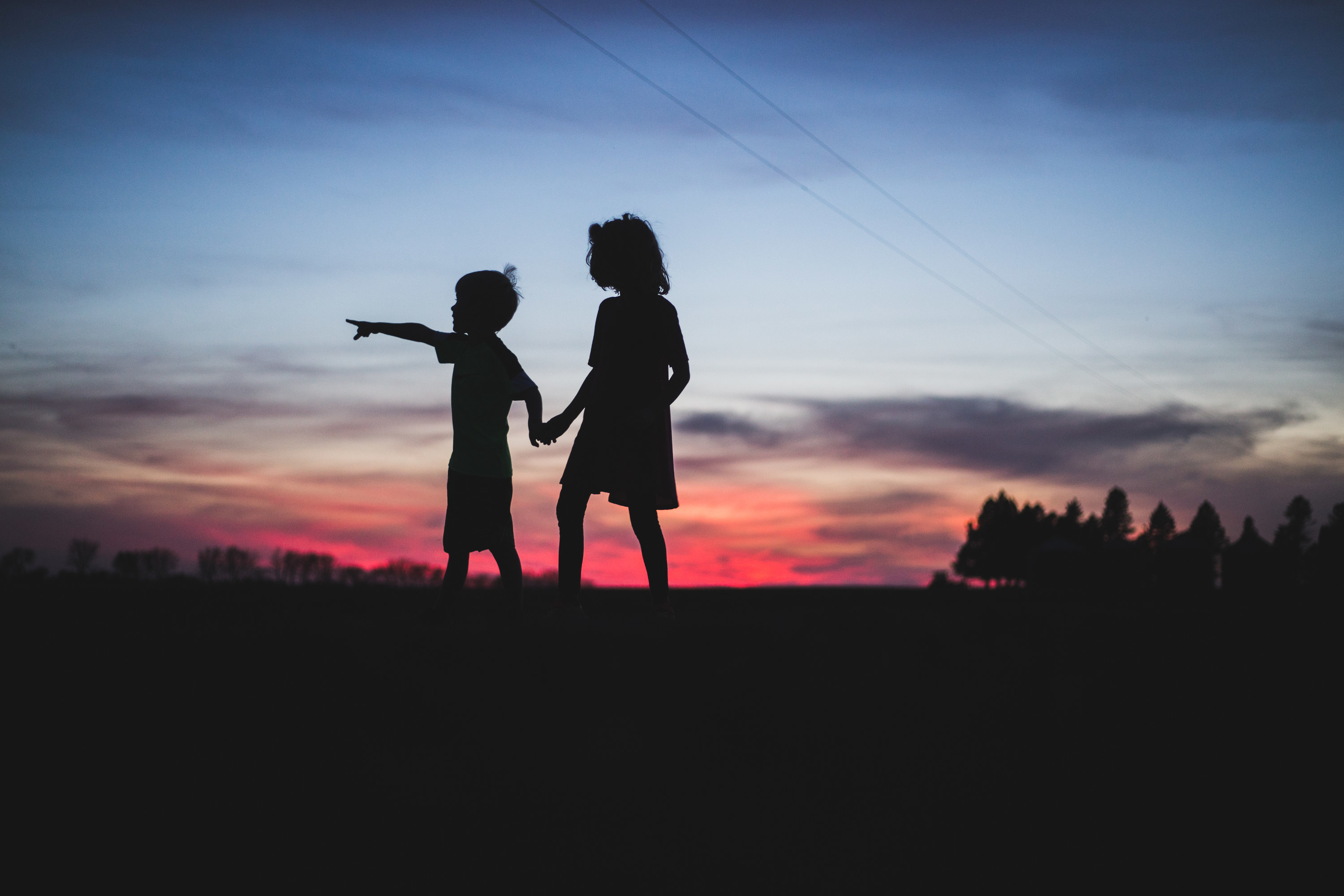 Two children hold hands as the sun sets behind them