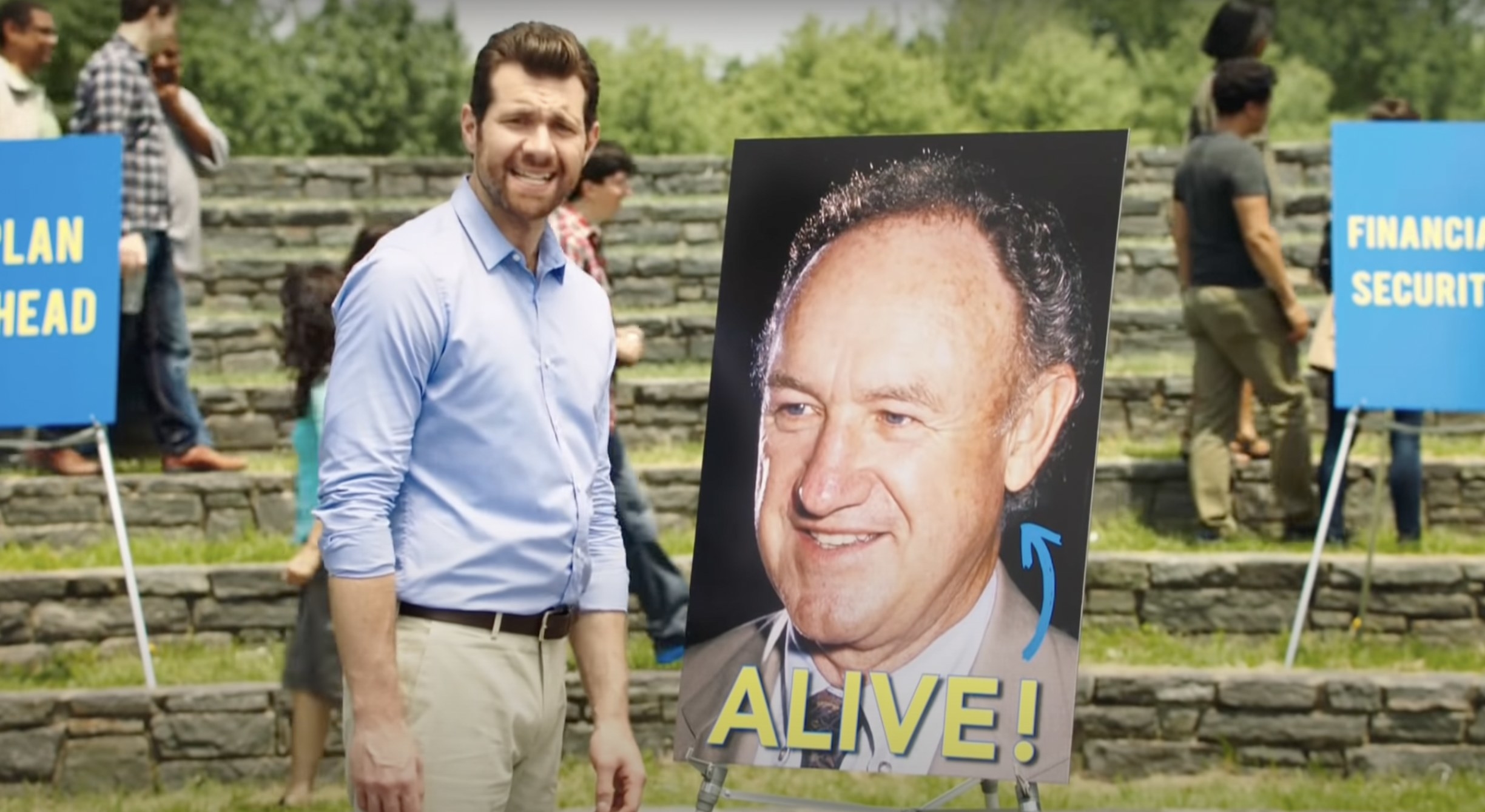 Billy Eichner standing in front of an image of Gene Hackman with ALIVE written under Hackmans face