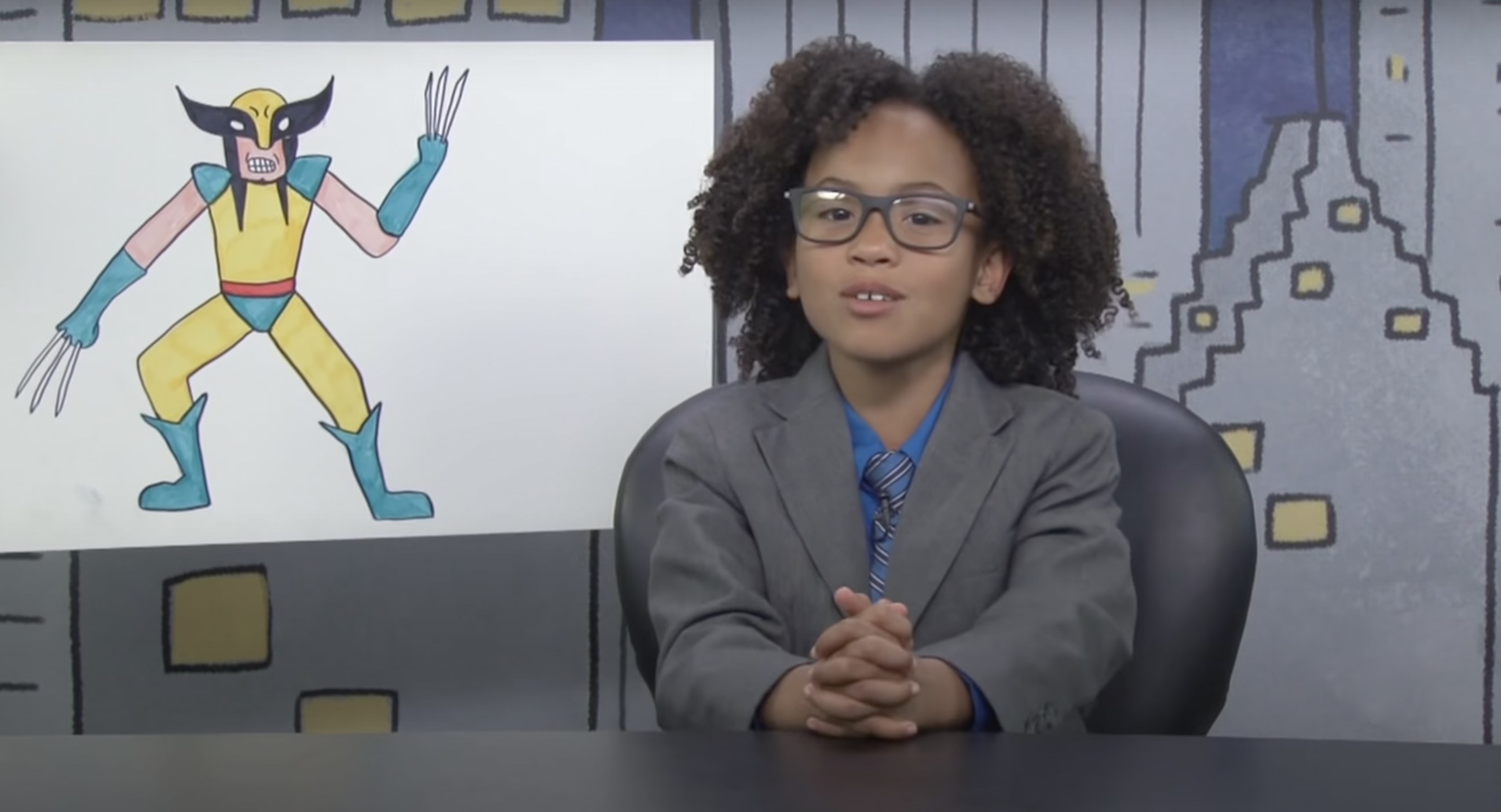 A child dressed up as John Oliver sitting at a desk with an drawing of Wolverine next to them