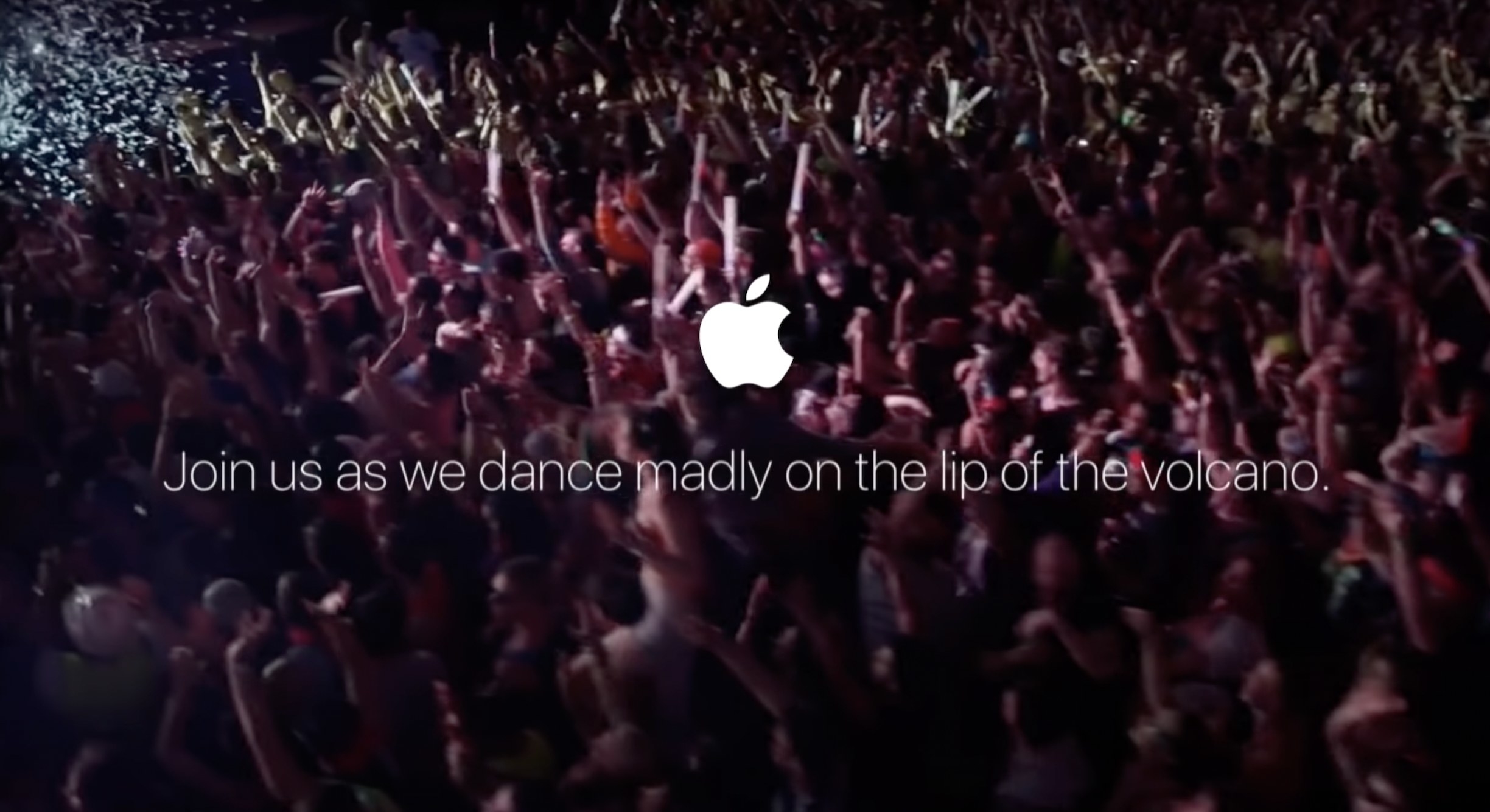 看起来像Apple添加的东西，在一个口号上的苹果徽标下方的人群的图像说，当我们疯狂地在火山的嘴唇上跳舞时，加入我们
