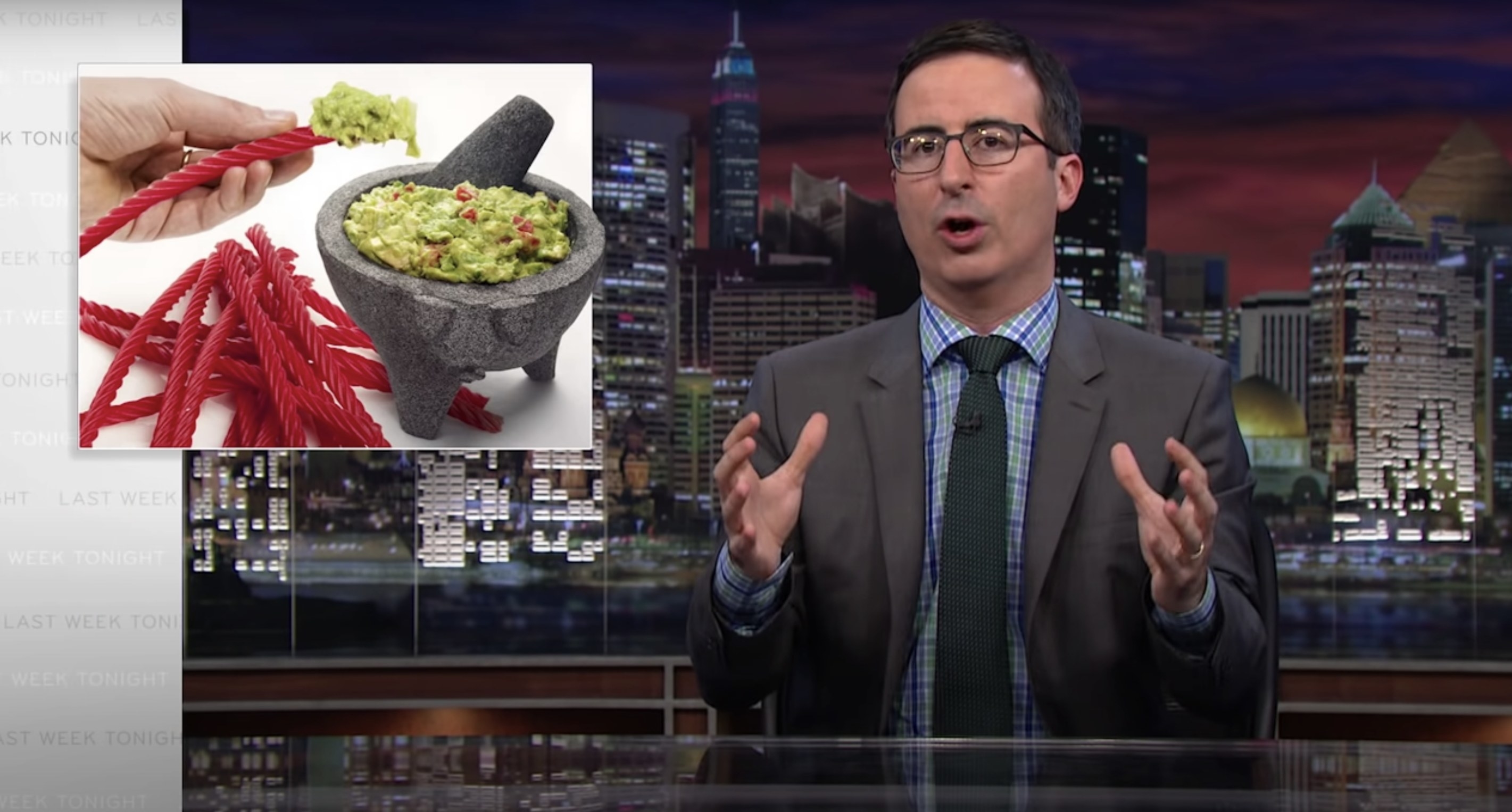 John Oliver at his desk, with an image of Twizzlers being dipped in guacamole next to him