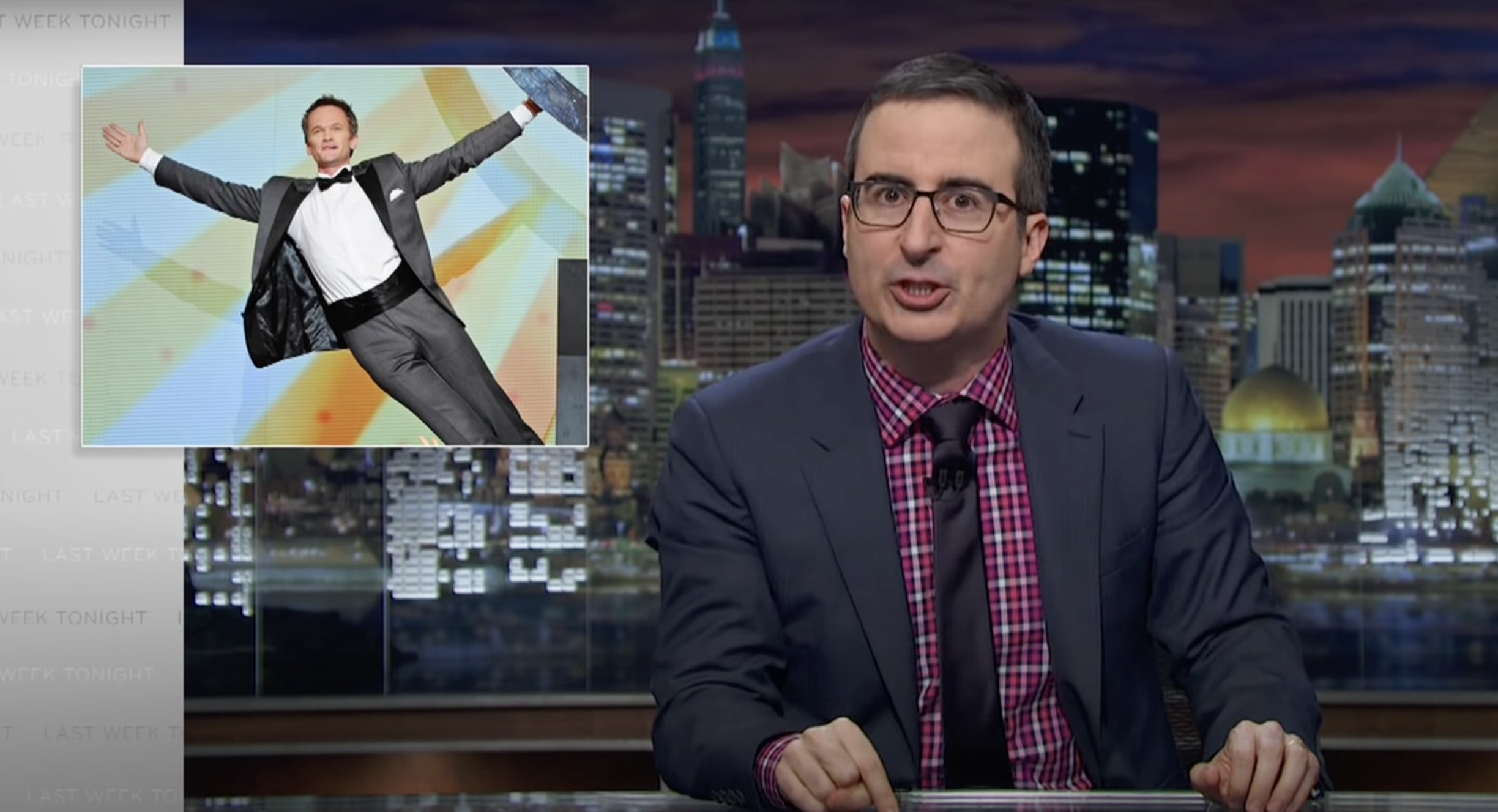 John Oliver at his desk passionately talking, with an image of Neil Patrick Harris next to him