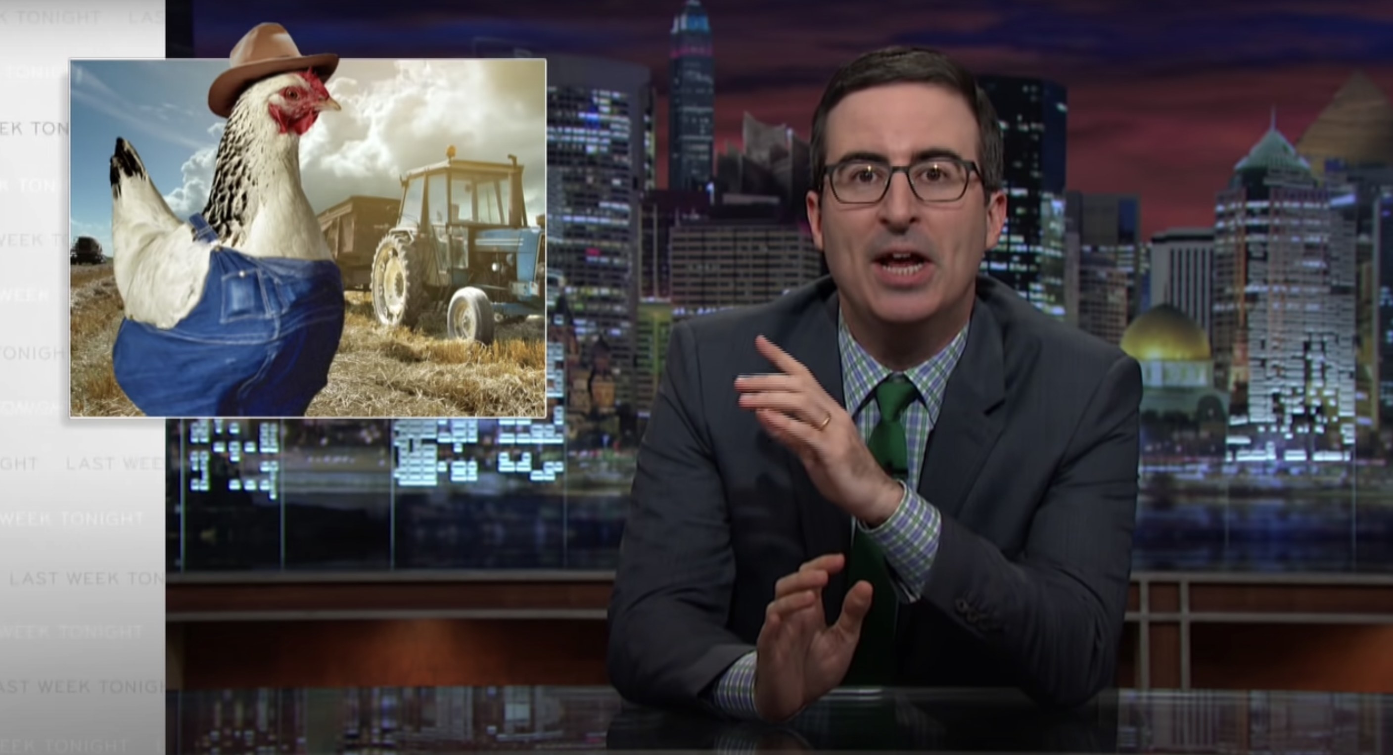 John Oliver at his desk, with an image of a chicken in overalls next to him