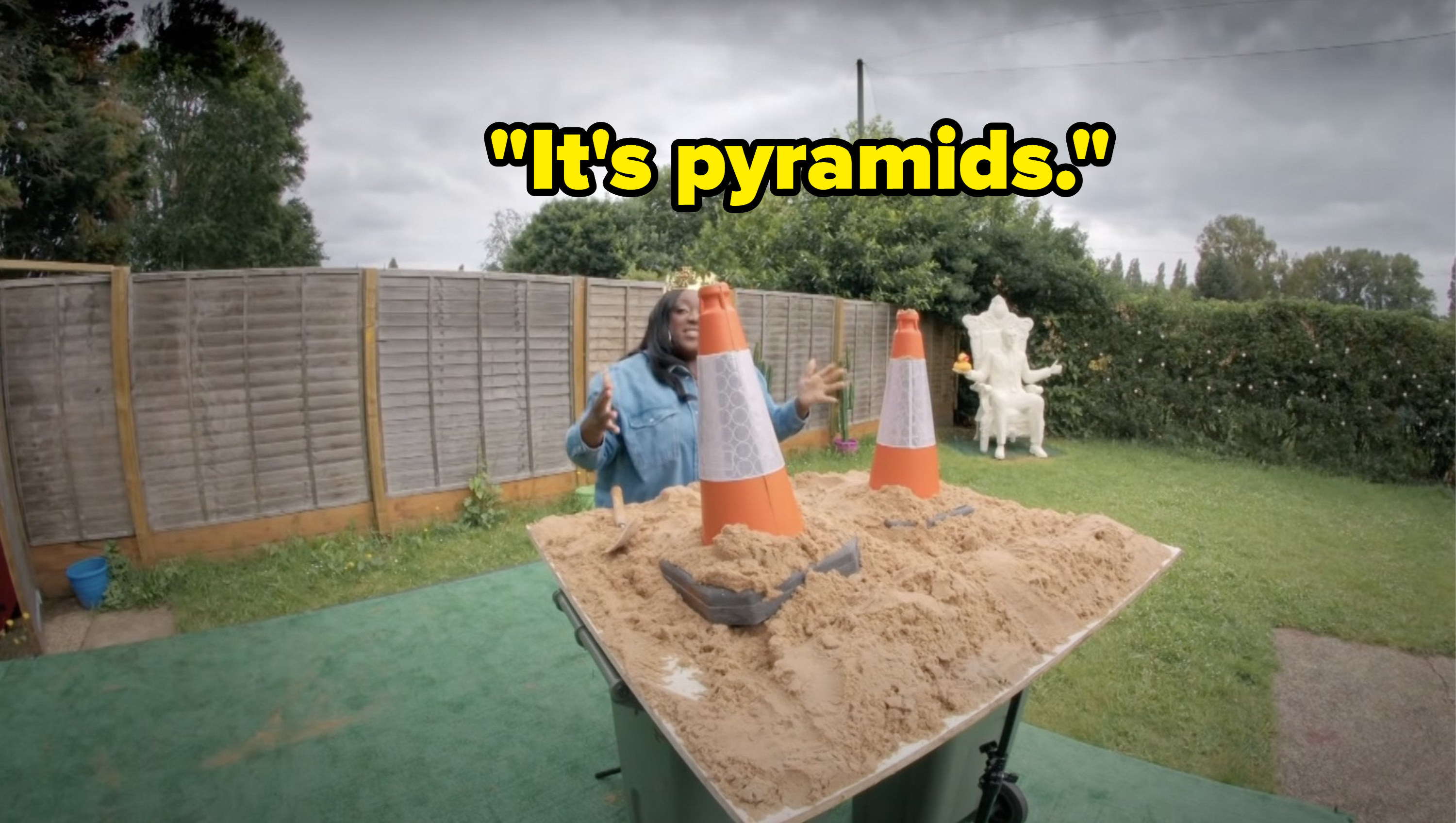 While standing in front of two traffic cones in sand, Judi Love says, Its pyramids