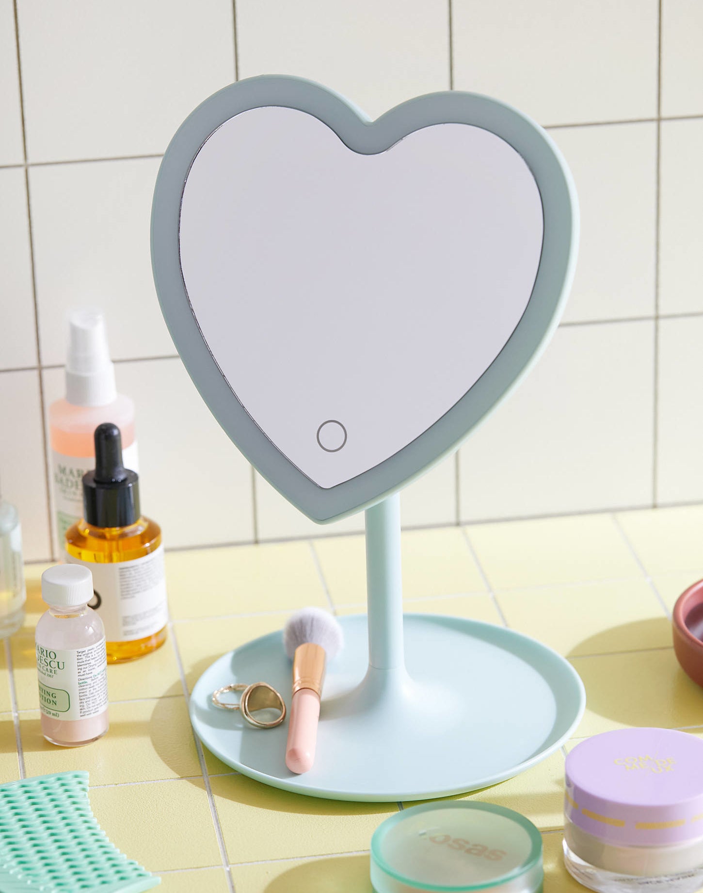 a heart-shaped LED mirror with a tray for toiletries on a counter