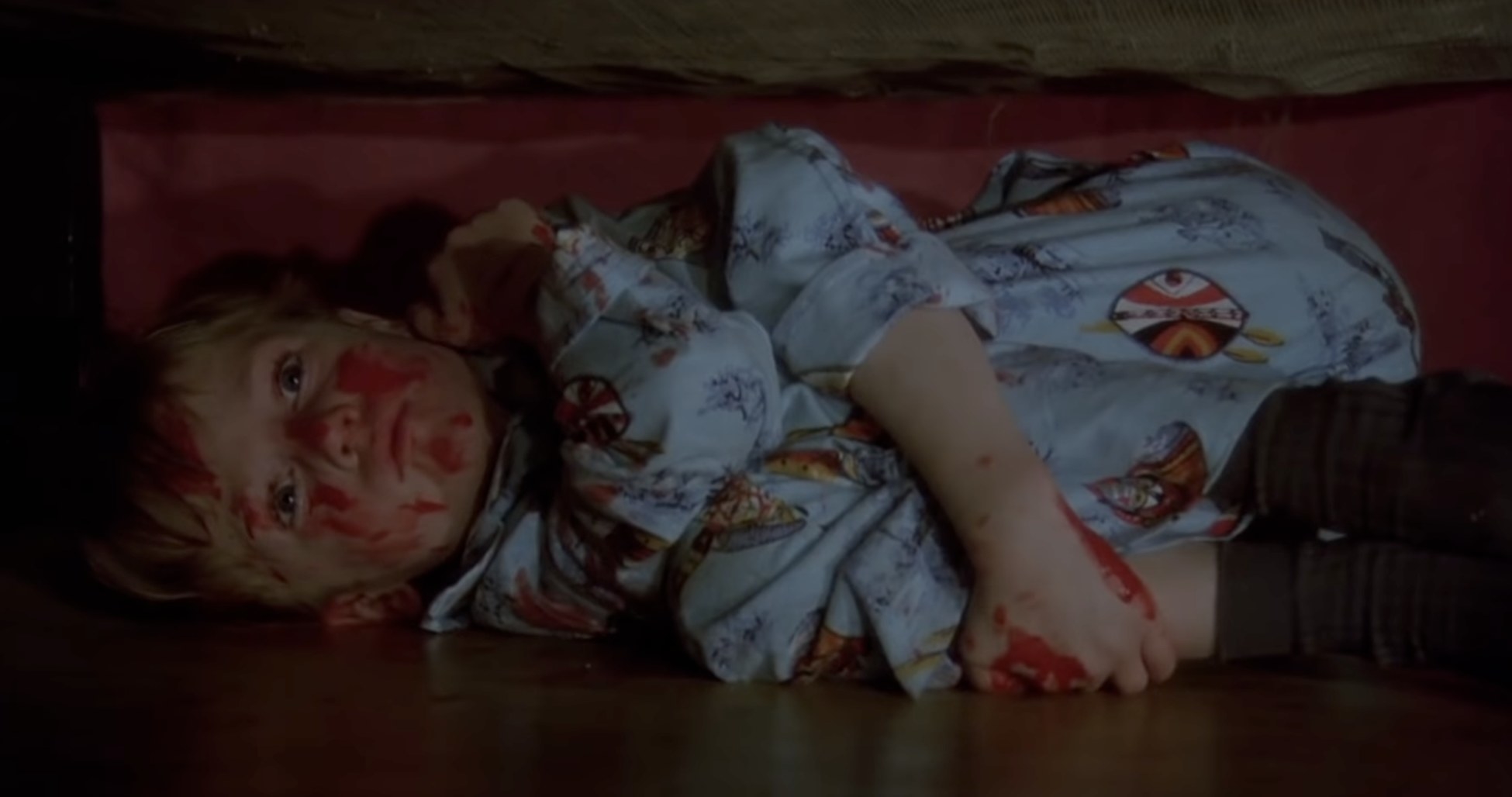a little boy covered in blood hiding under a bed