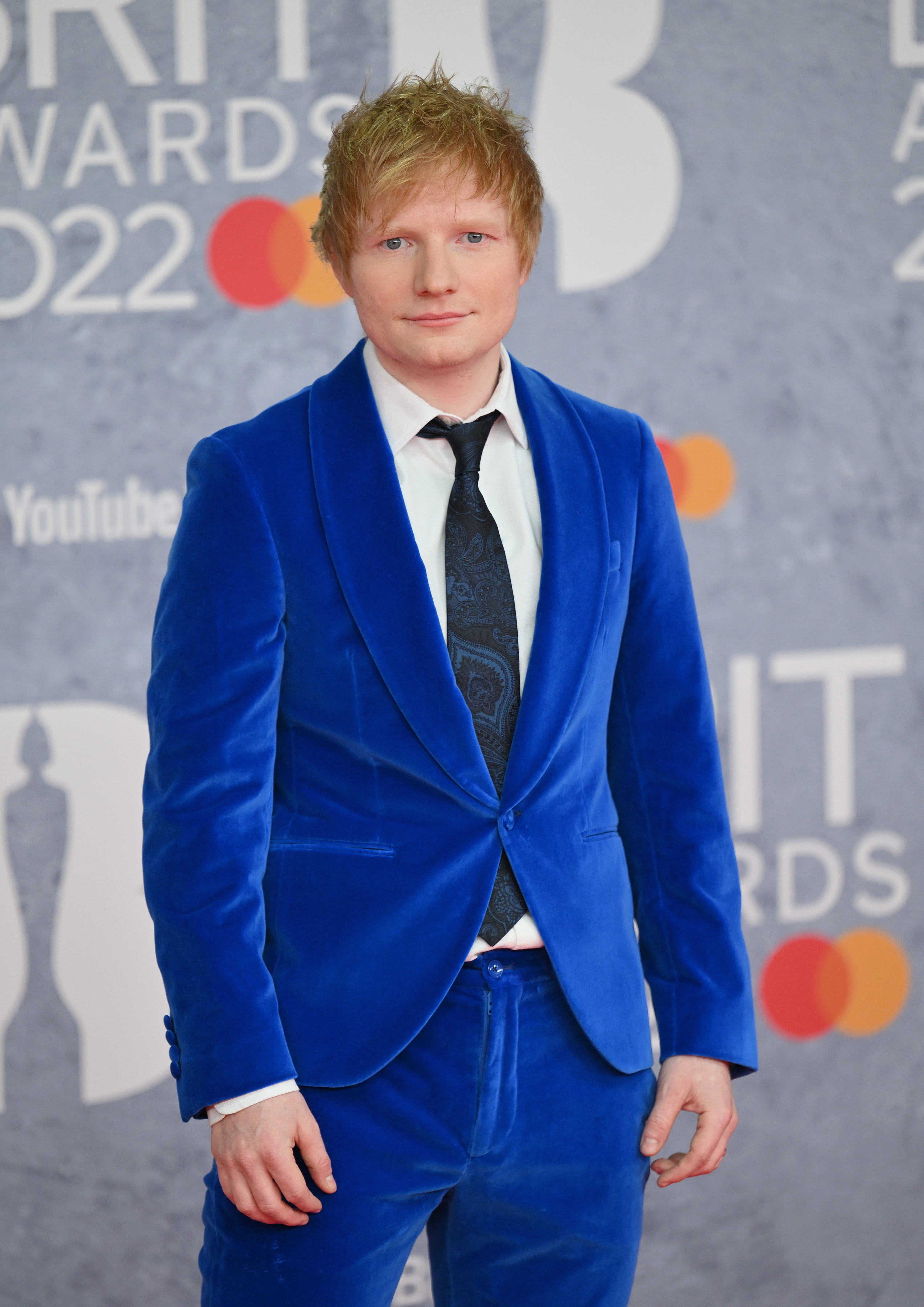 ed sheeran posing in a blue suit on a red carpet