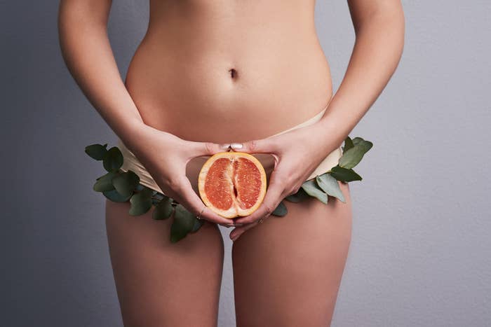A woman holding a halved grapefruit over her pelvic region