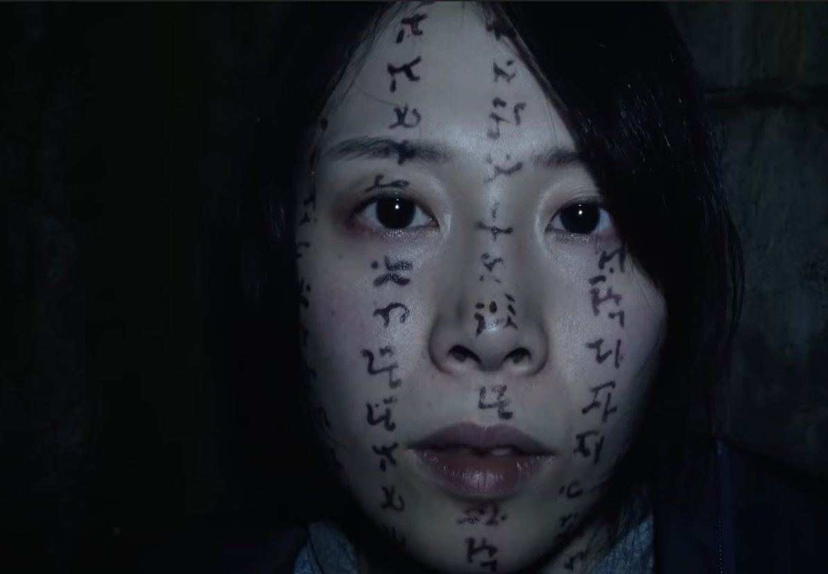 A woman stands in the dark with symbols all over her face