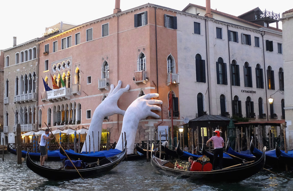 giant hands emerging from venice canals and holding onto a wall