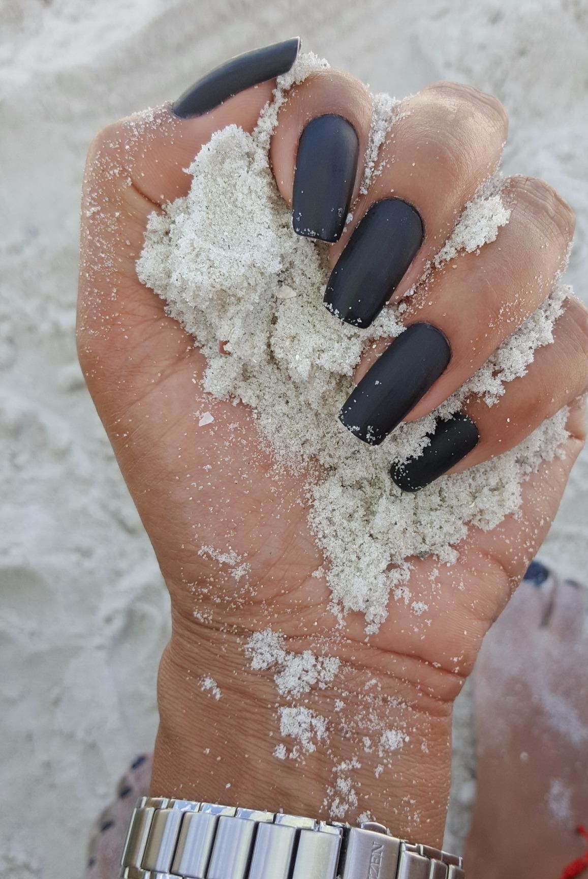 Reviewer showing matte mani while holding sand on the beach