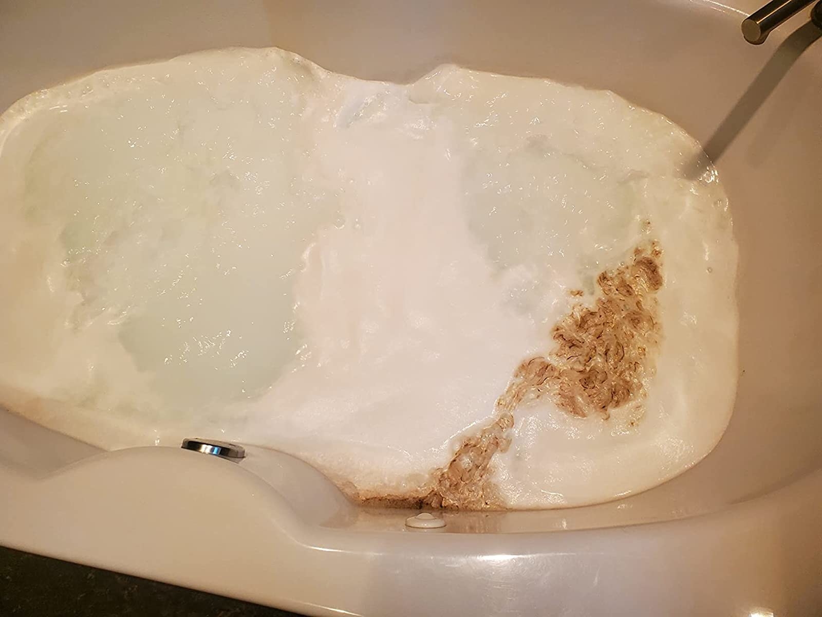a reviewer photo of a jetted tub with brown gunk floating in the water