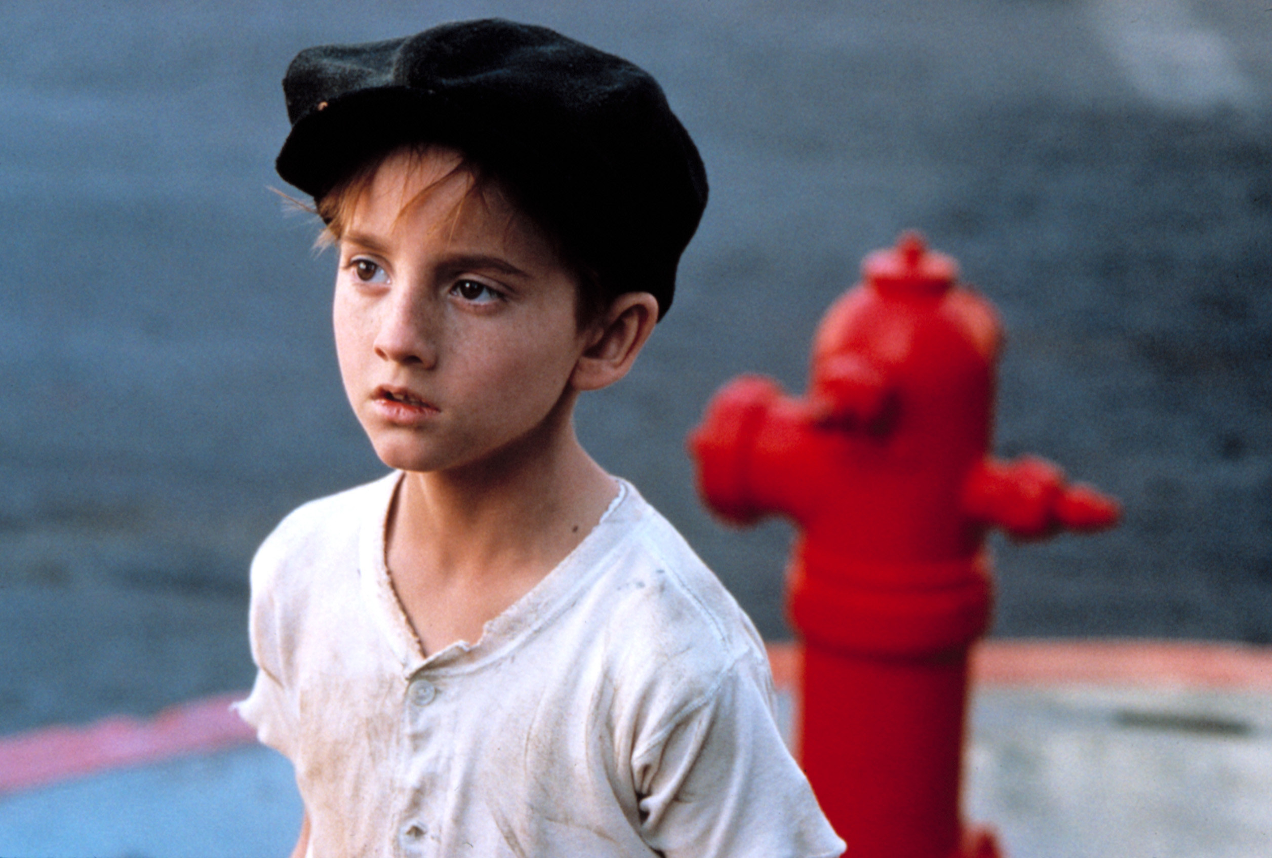 Charlie as a child wearing a cap and standing in front of a fire hydrant
