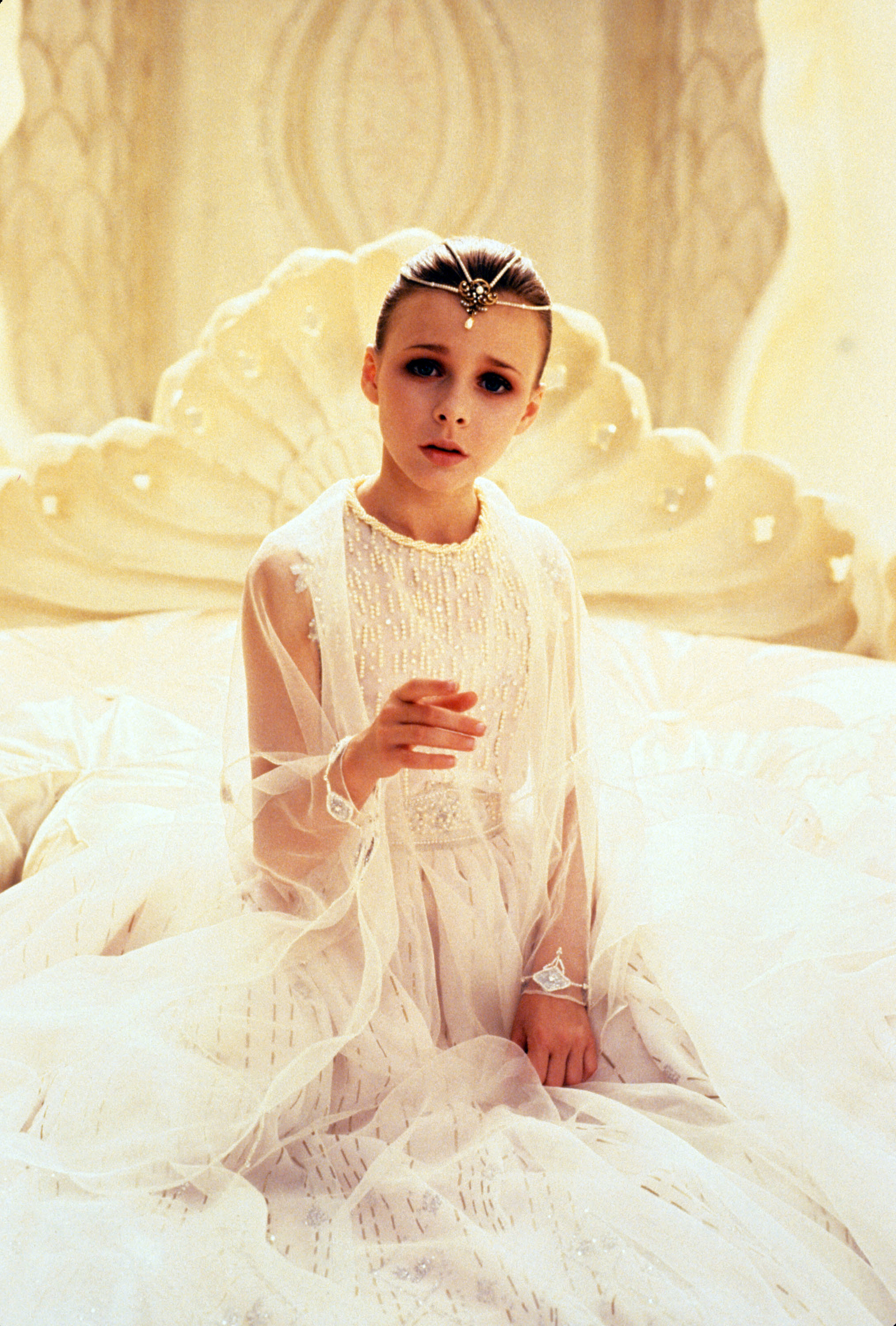Tami as a child sitting on a lavish bed in a gauzy, bejeweled outfit