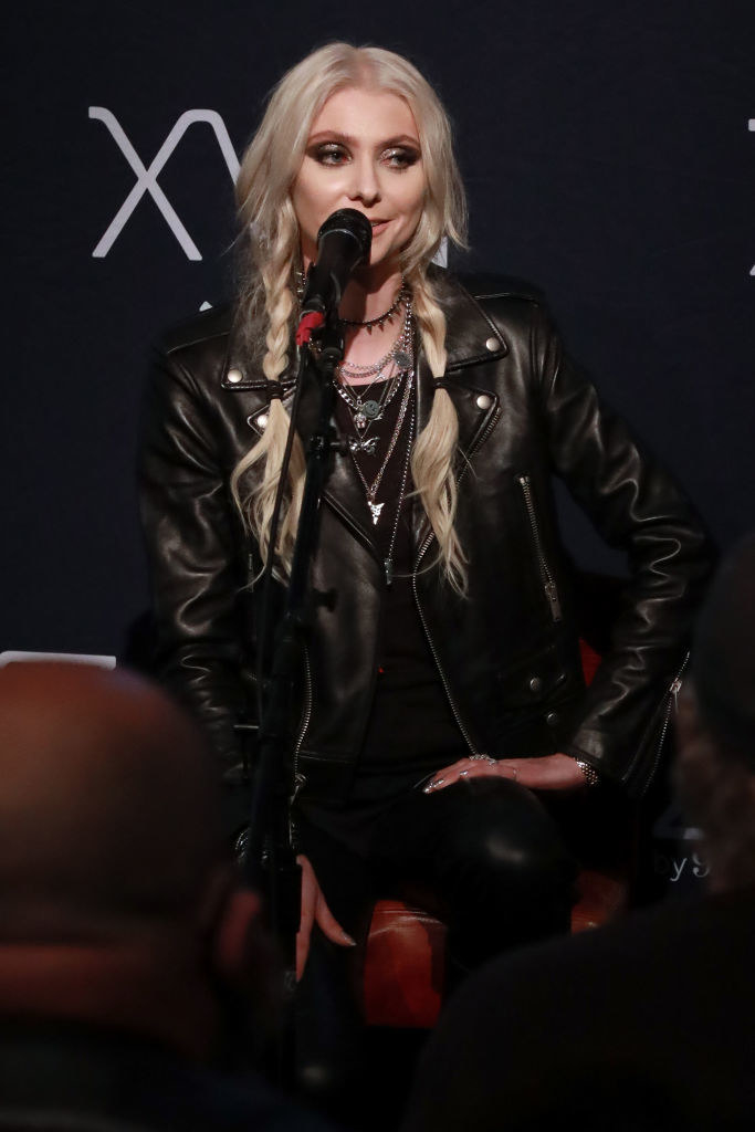 Taylor as an adult wearing a leather jacket and speaking into a microphone