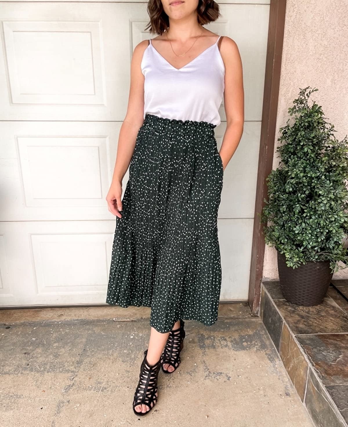 Reviewer wearing dark green polka dot skirt with black sandals and white tank top