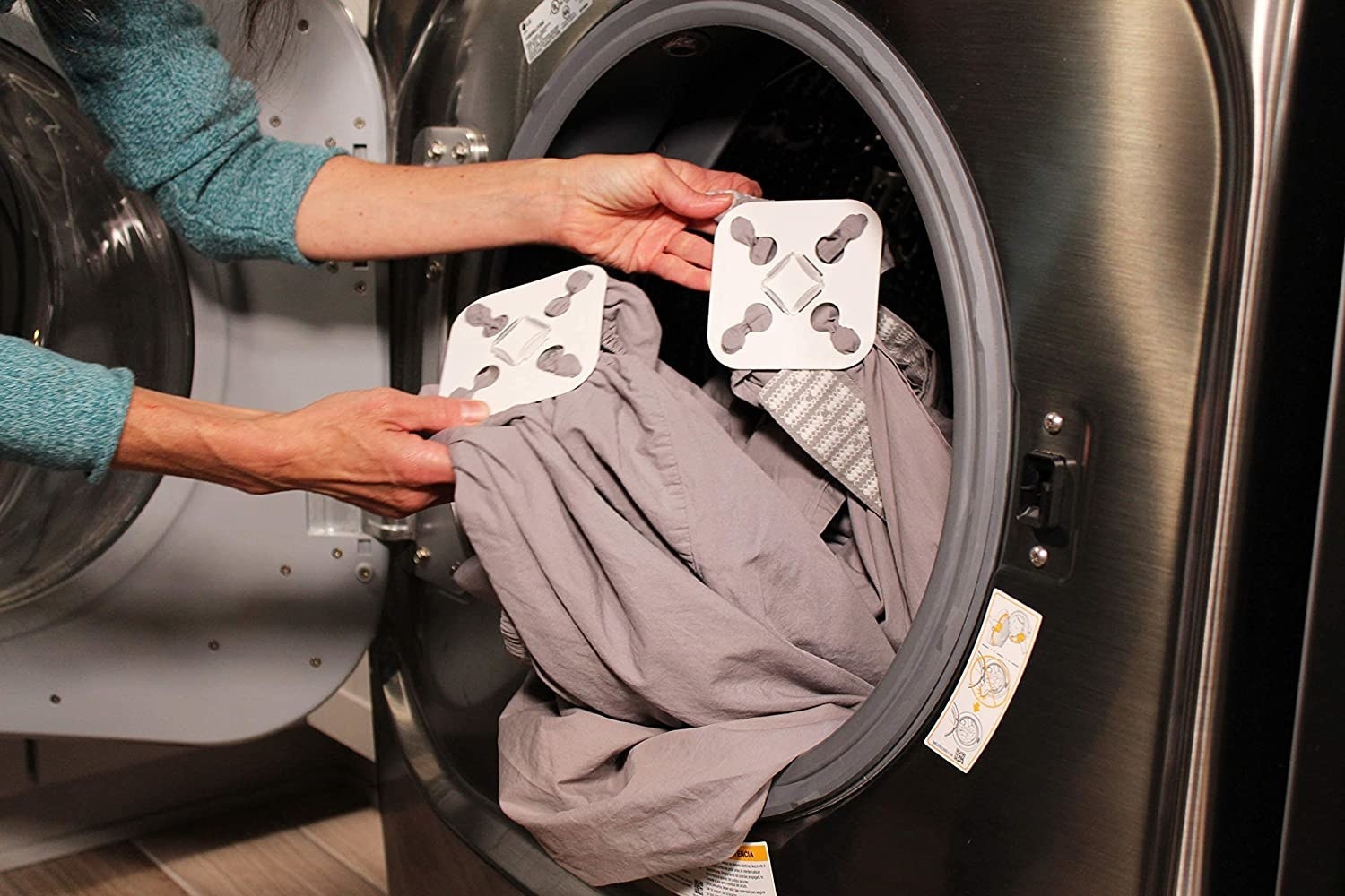 a model holding a set of grey sheets with the wad preventer attached as it goes into the dryer
