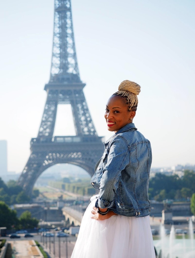 Reviewer wearing denim jacket over white dress in front of Eiffel tower