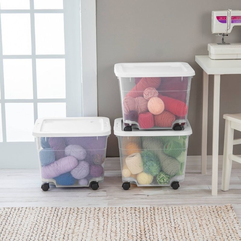 three white and clear rolling storage boxes containing yarn