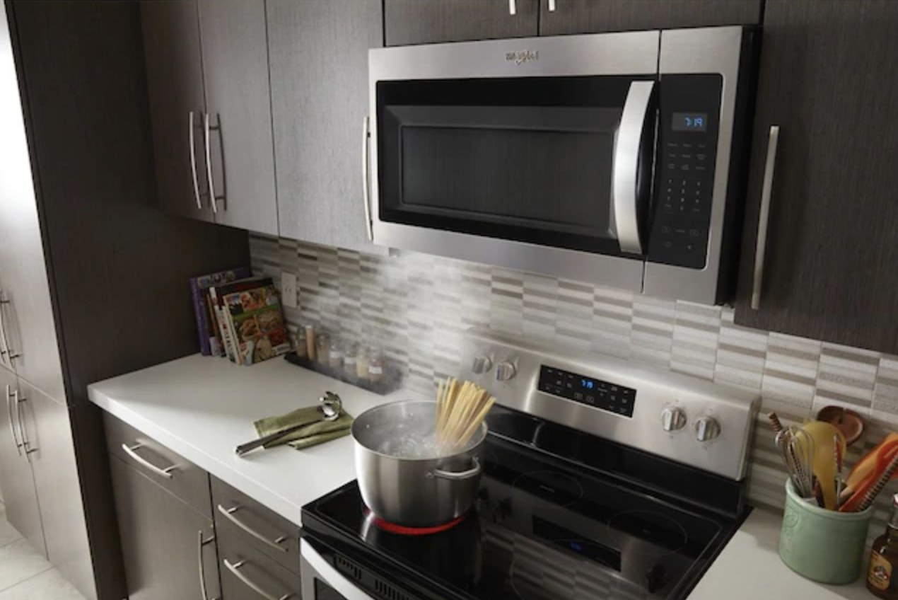 the microwave installed above stovetop with pot of noodles cooking beneath
