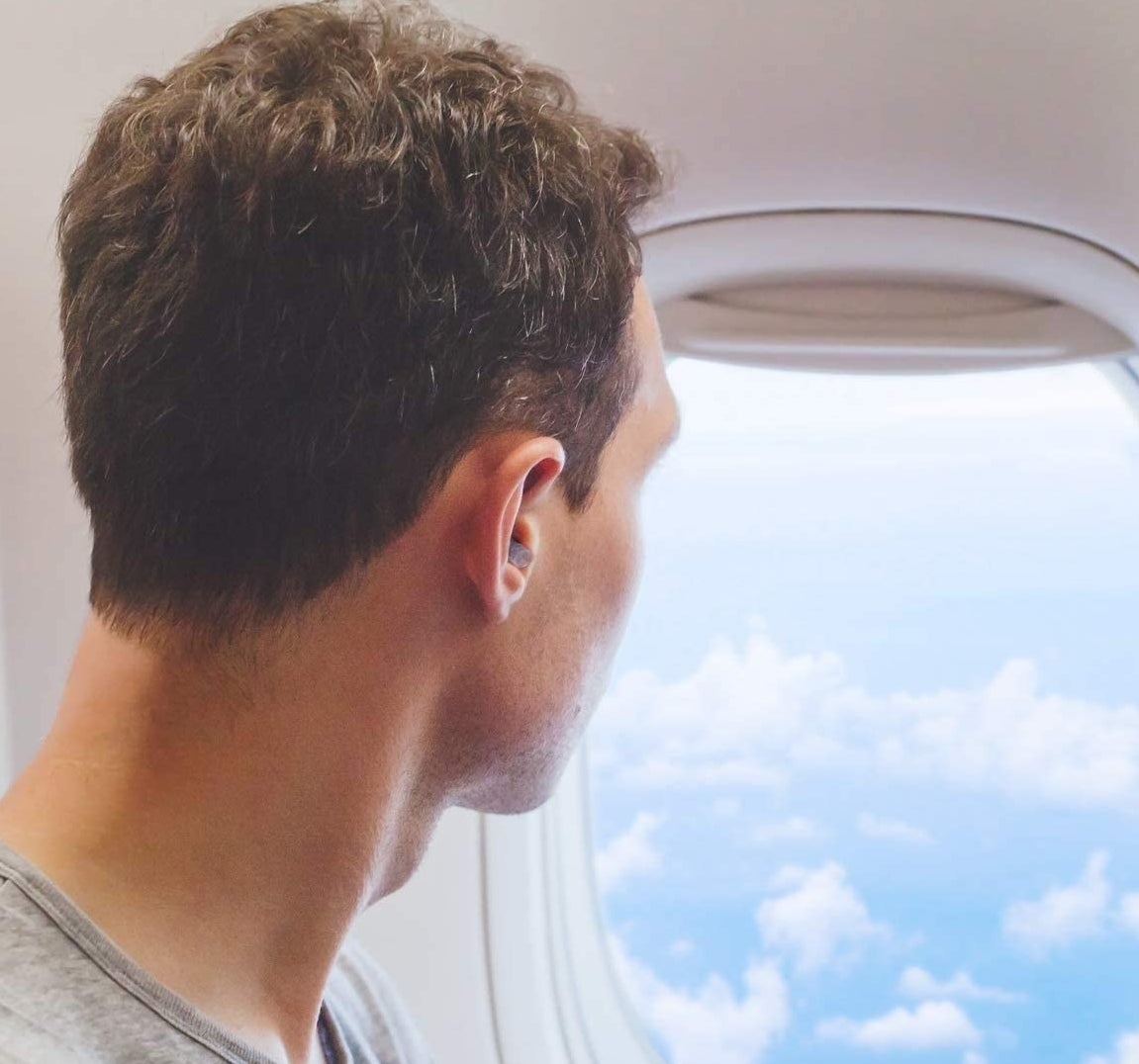 Someone wearing the earplugs on a plane while looking out the window