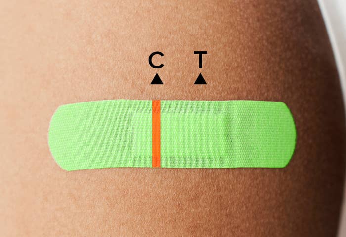 A bright green bandaid on a shoulder. There is a single orange line on the bandaid as if the bandaid is a Covid-19 test. There is a C for control and a T for test. The single line means that the test is negative.