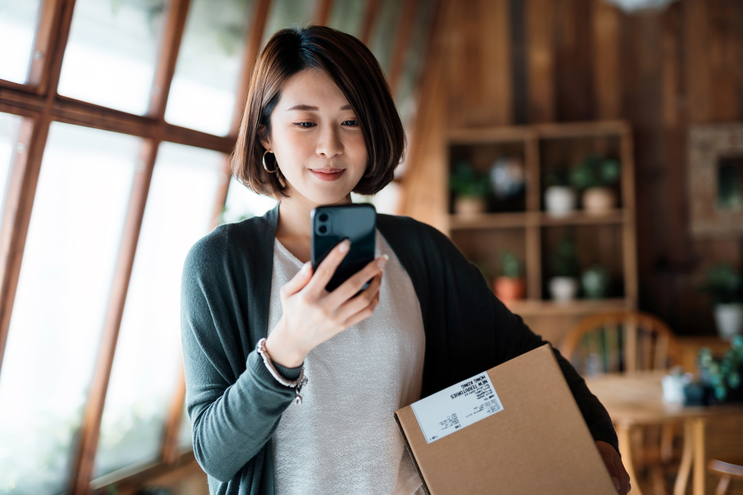 A woman looking at a phone while she holds a box