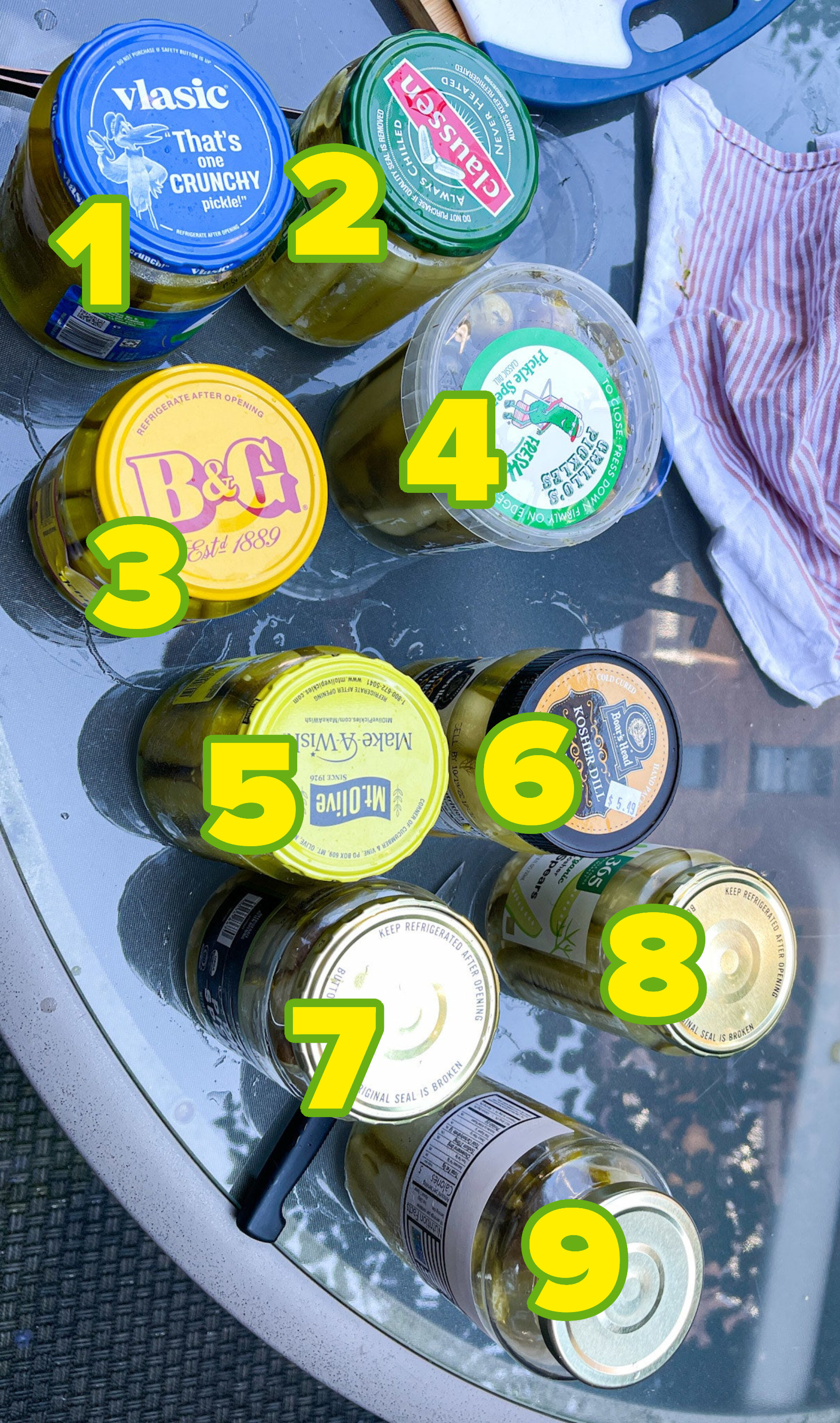 Nine assorted pickle jars labeled with numbers on a glass table
