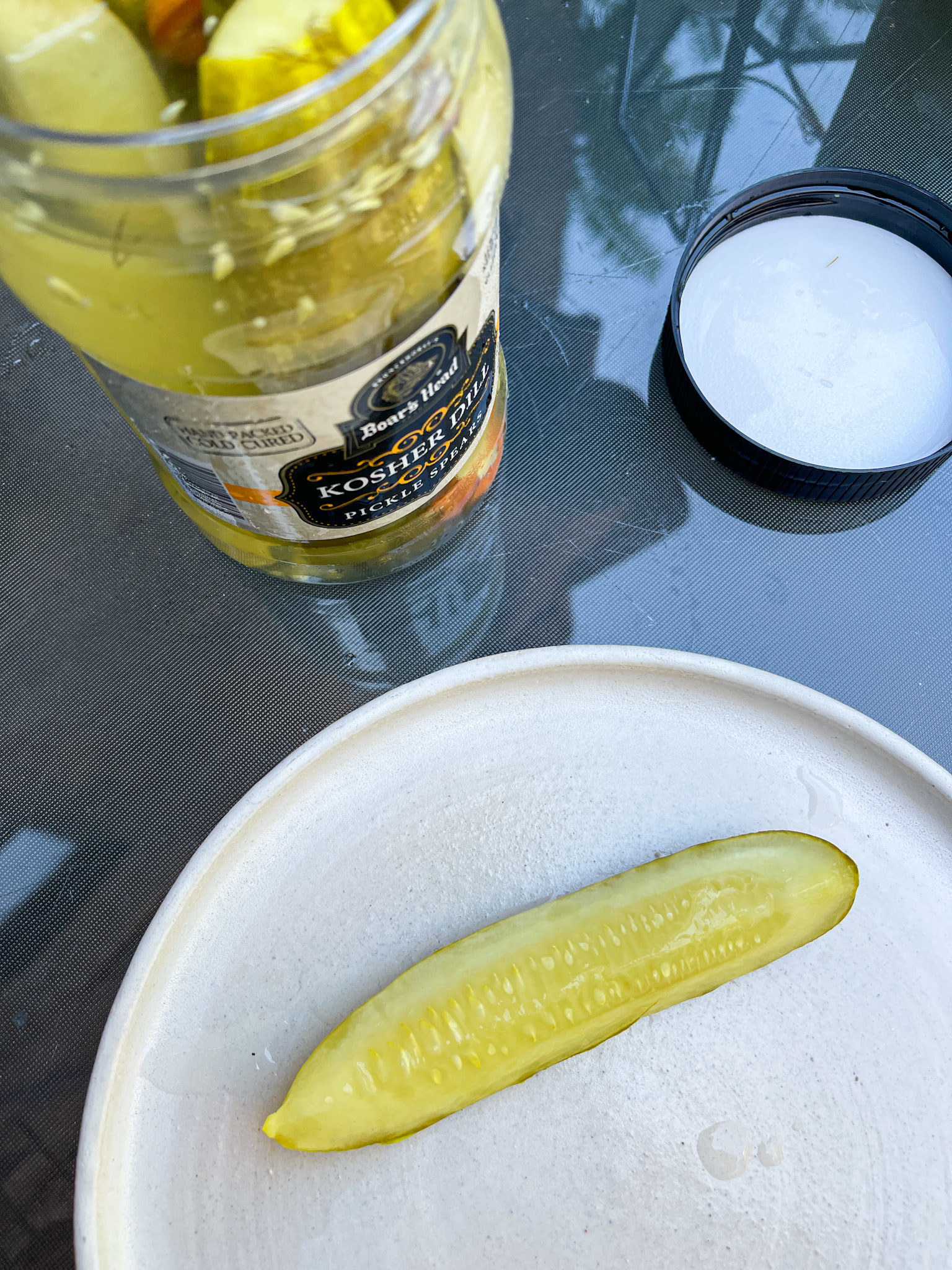 A pickle slice on a plate beside an open jar of pickles on a table