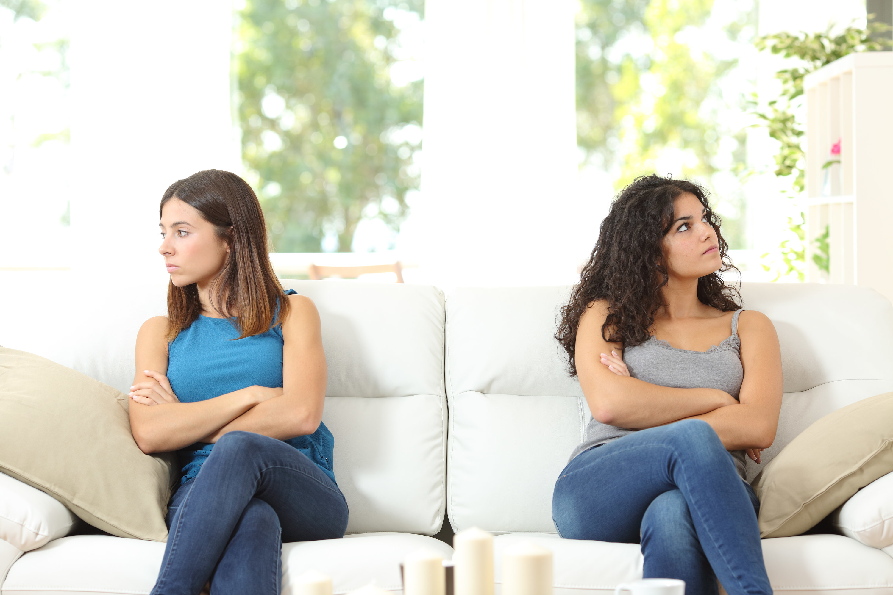 Two women coldly look away from one another while sitting next to each other on a couch
