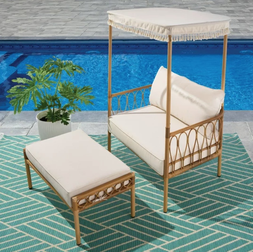 Wicker canpoy chair and ottoman with white cushioning in front of pool