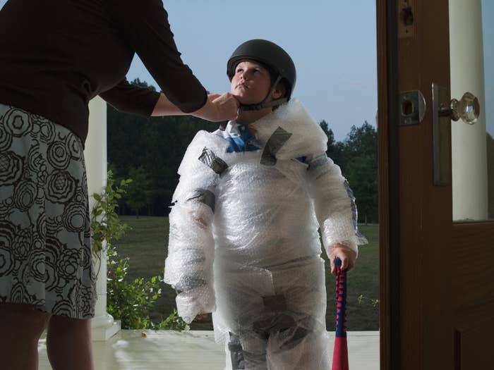 a woman putting a helmet on a kid who is wrapped in bubble wrap