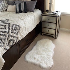 the white faux fur rug on the floor beside a reviewer's bed