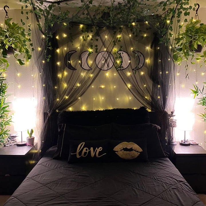 a black canopy strung up around a different reviewer's bed with fairy lights and plants all around
