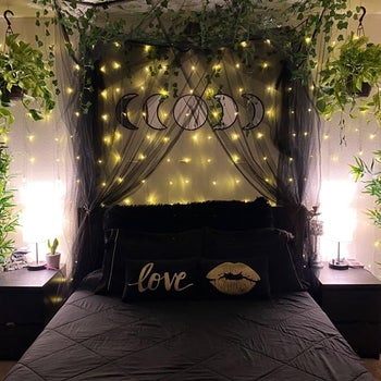 a black canopy strung up around a different reviewer's bed with fairy lights and plants all around