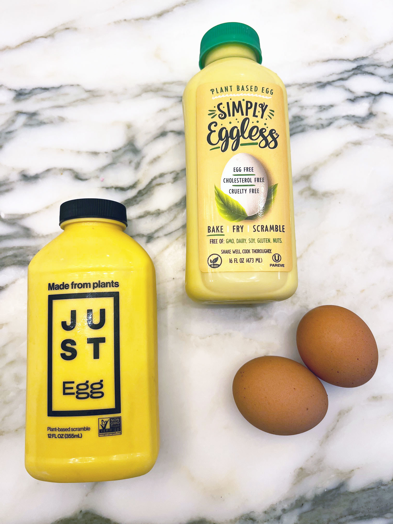 Two plant-based egg alternatives next to two eggs.