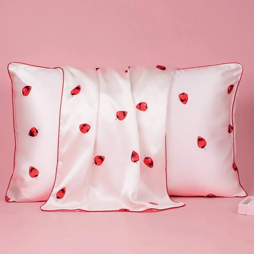 A pillow with a light pink silk pillowcase that has a strawberry print