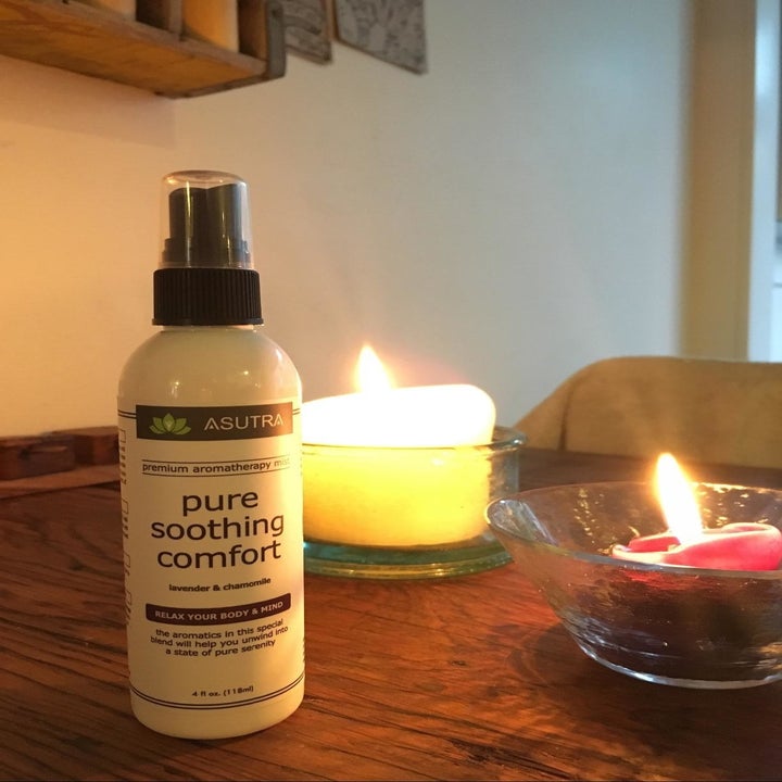 the asutra essential oil spray on a table next to burning candles