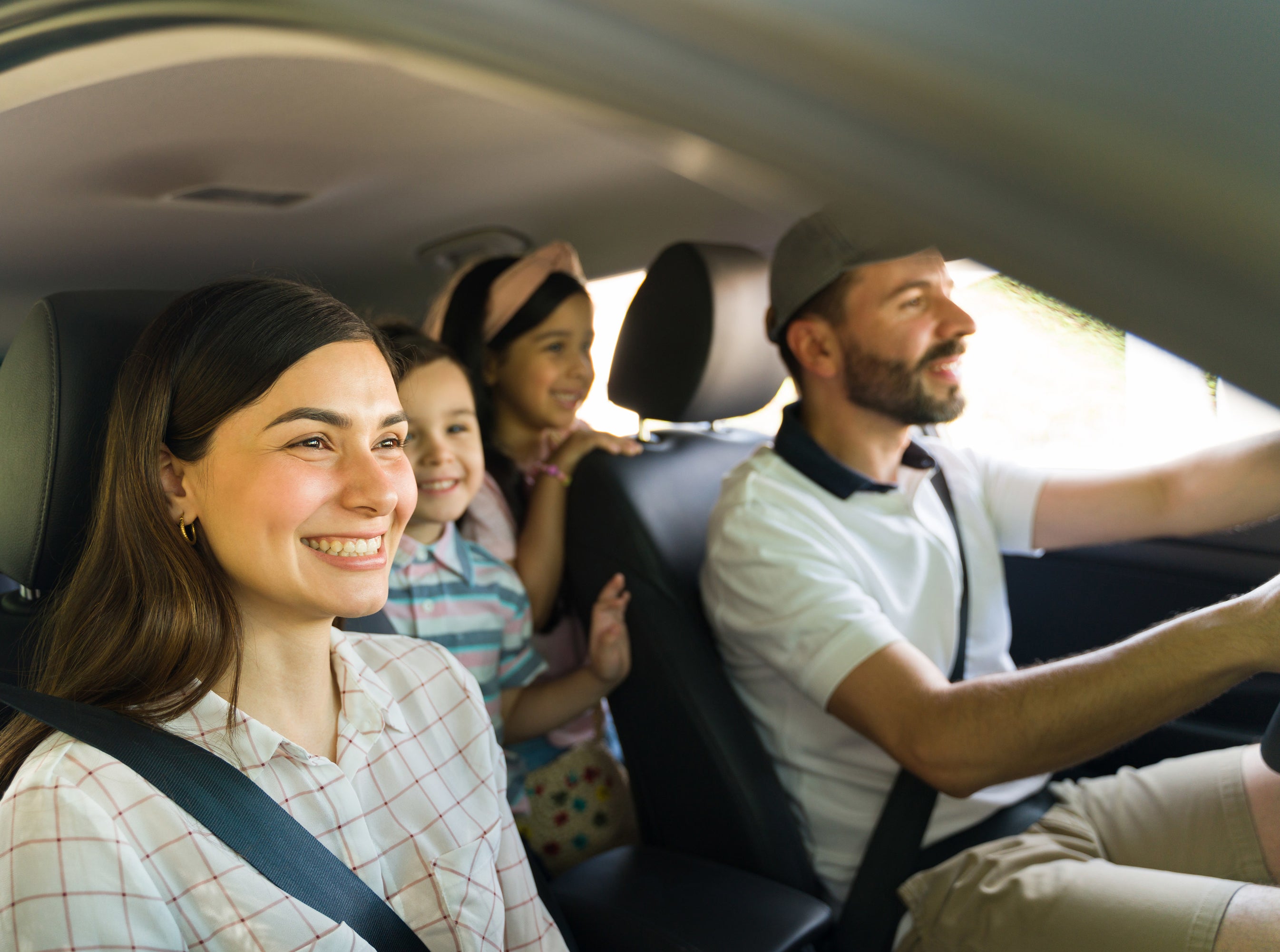 A couple and their kids smiles as they embark on a road trip together