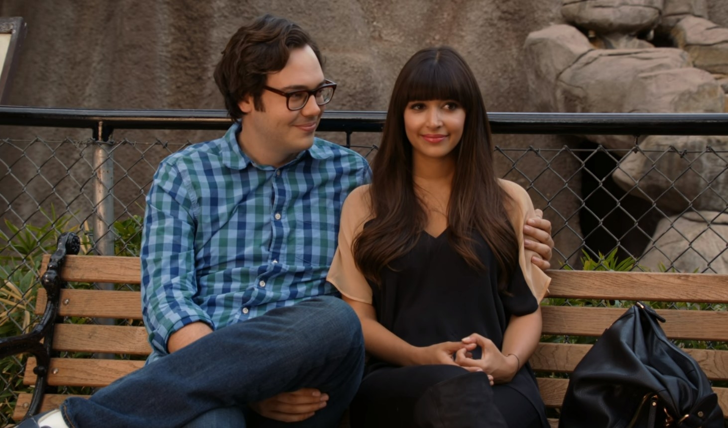 Robby puts an arm around Cece as they sit on a park bench
