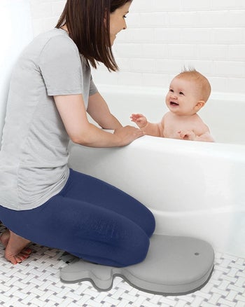 A parent on kneeling on the whale-shaped bath pad
