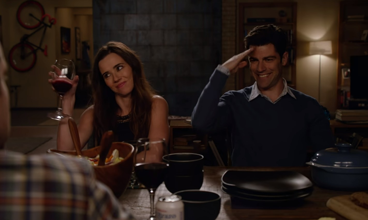Abby raising a glass of wine while Schmidt sits next to her and salutes