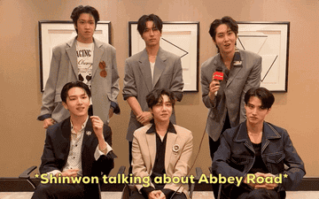 PENTAGON sat in an interview room and Shinwon (신원) is reenacting his time at Abbey Road where he posed for photos on the crossing All the other members are nodding and Kino (키노) is smiling widely