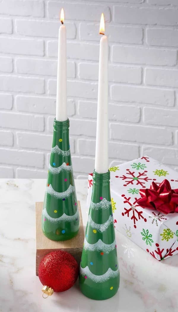 Long bottles decorated to look like green trees with tinsel and holding candles